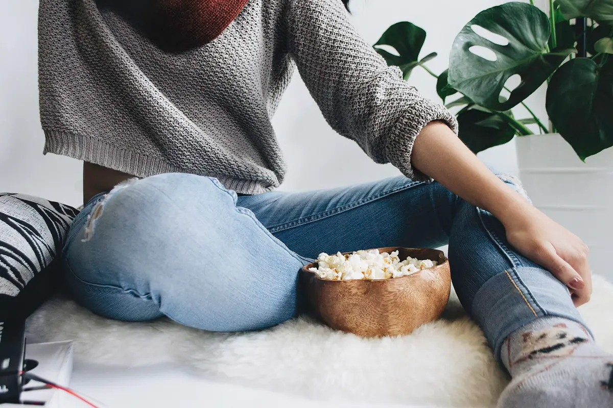 Person in jeans and a knit sweater relaxing on a soft white sheepskin rug with a bowl of popcorn