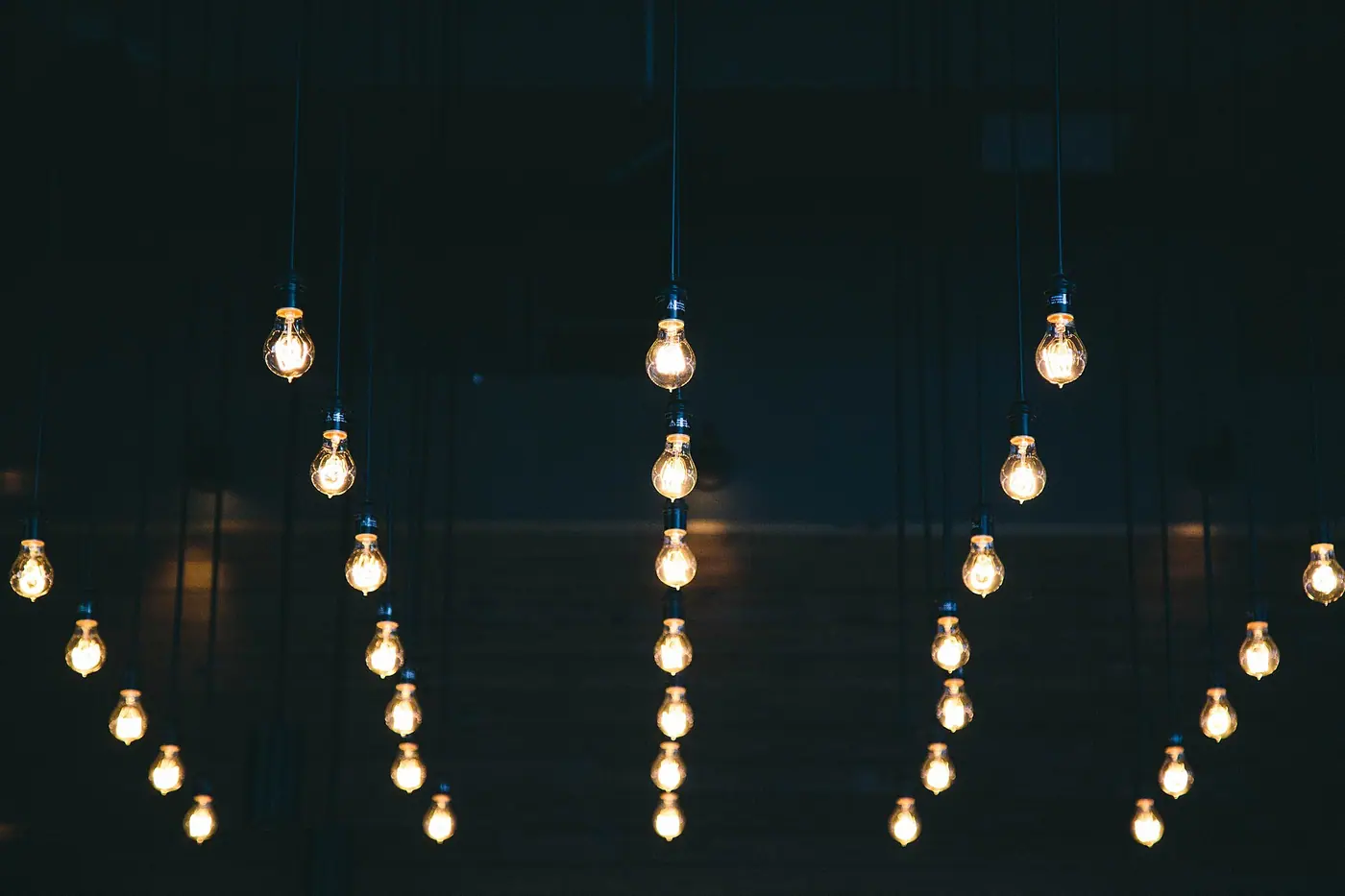Rows of glowing filament light bulbs hanging against a dark background