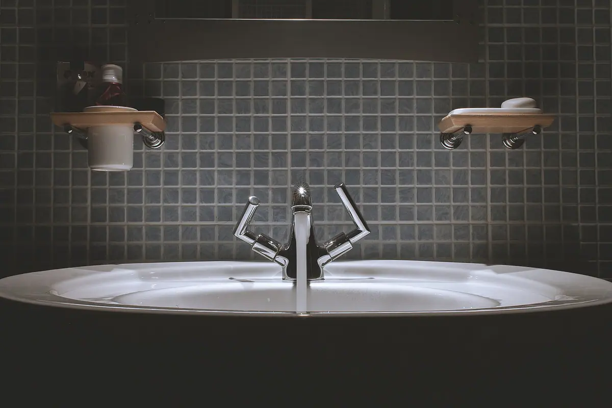 Chrome faucet running water into a white basin against dark mosaic tile