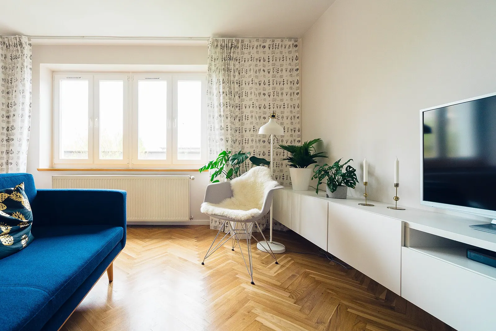 Bright modern living room with a blue sofa, white media cabinet, houseplants and herringbone wood floor