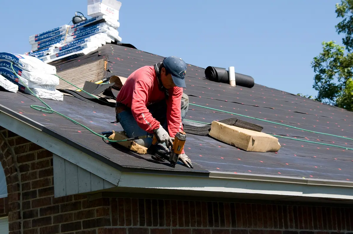 Roofer kneeling on underlayment using a nail gun on a residential roof