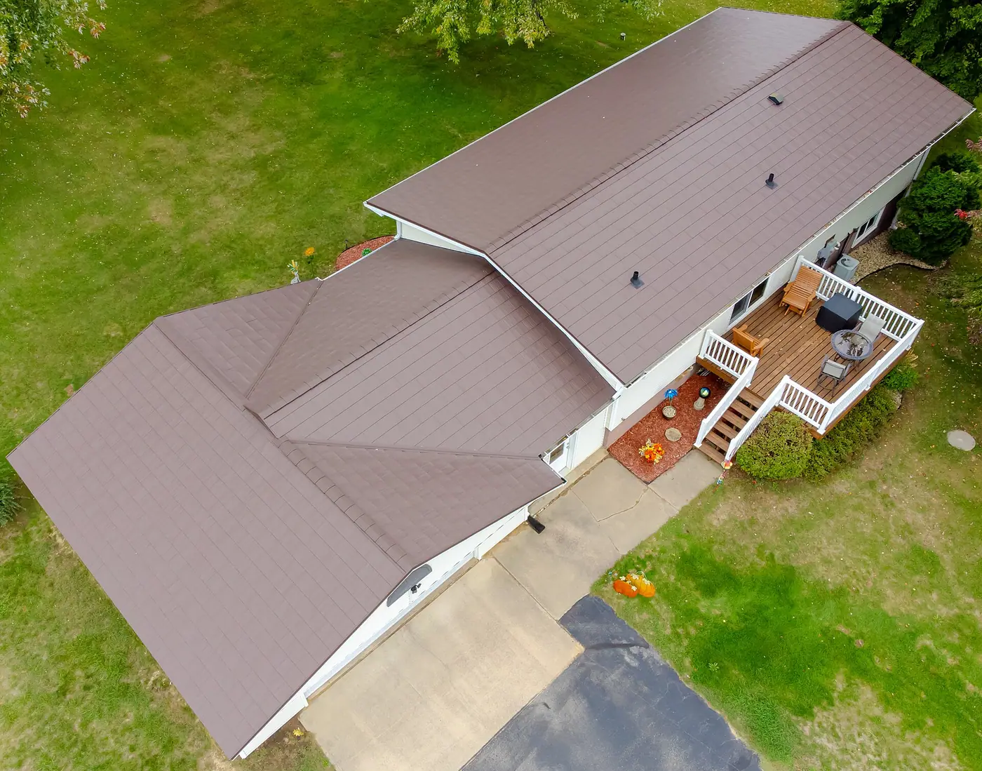 Aerial view of a ranch house with a new brown shingle-style roof, deck and green lawn